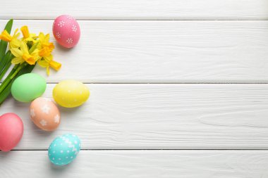 Boyanmış Paskalya yumurtaları ve beyaz ahşap masa üzerinde güzel nergisler. Metin için boşluk
