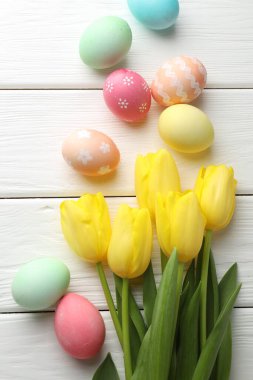 Boyanmış Paskalya yumurtaları ve beyaz ahşap masada güzel laleler, düz uzanmış.