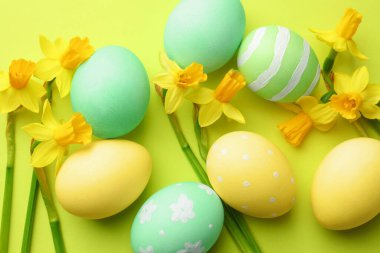 Boyanmış Paskalya yumurtaları ve açık yeşil arka planda güzel nergisler.