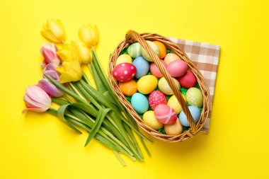 Sarı arka planda boyanmış yumurtalar ve laleler olan Paskalya sepeti düz yatıyordu.