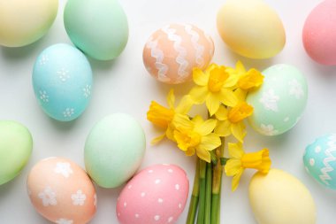 Beyaz arka planda boyanmış Paskalya yumurtaları ve güzel nergisler.