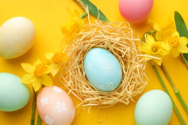 Boyanmış Paskalya yumurtaları ve turuncu arka planda güzel nergisler.