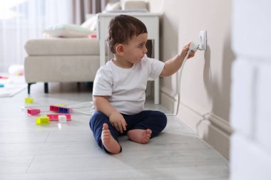 Evde çocuk güvenliği. Küçük çocuk içerideki elektrik prizinin fişini çekiyor.