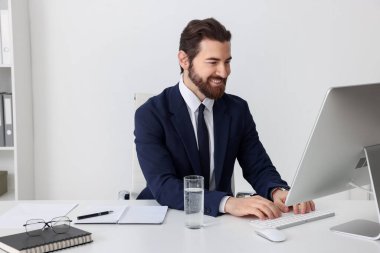 Beyaz duvarın yanındaki masada bilgisayarla çalışan bir işadamı.