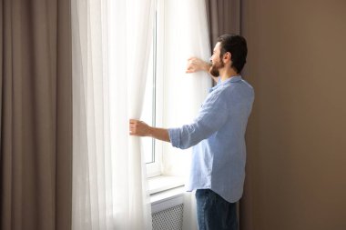 Evde şık pencere perdeleri açan adam