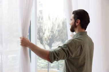 Evde şık pencere perdeleri açan adam