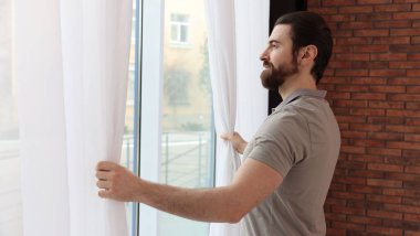 Evde şık pencere perdeleri açan adam