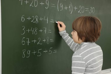 Okullu çocuk sınıfta tahtada matematik yapıyor.