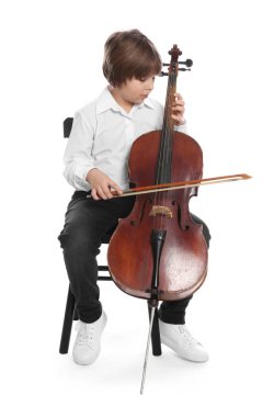 Küçük çocuk beyaz arka planda sandalyede keman çalıyor.