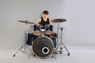 Gri arka planda davul çalmayı öğrenen güler yüzlü genç çocuk.