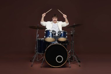 Davul çalan mutlu ergen çocuk kahverengi arka planda davul çalmayı öğreniyor