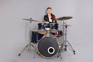 Açık gri arka planda bagetleri ve davulları olan genç bir kız.