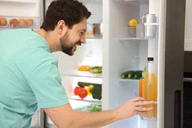 Mutfakta farklı gıda ürünleri olan açık buzdolabının yanındaki adam.