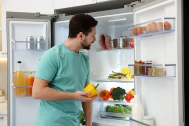 Mutfaktaki açık buzdolabının yanında dolmalık biberli adam var.