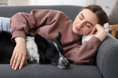 Evdeki kanepede uyuyan sevimli köpeğiyle genç bir kadın.