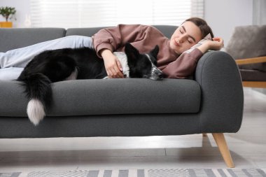 Evdeki kanepede uyuyan sevimli köpeğiyle genç bir kadın.