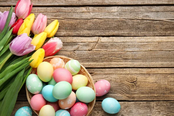 Hasır sepete boyanmış Paskalya yumurtaları ve ahşap masa üzerinde güzel laleler. Metin için boşluk