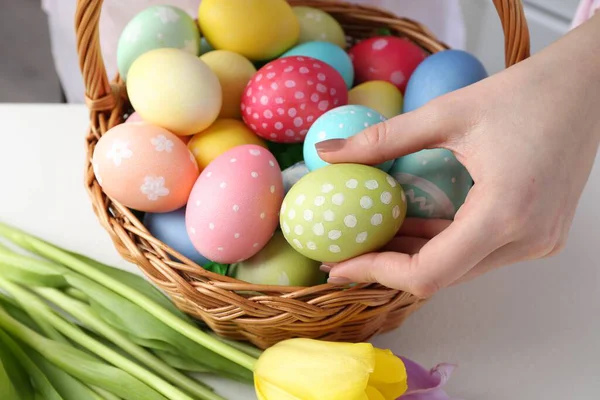 Paskalya sepetinde yumurta boyalı bir kadın ve beyaz masa içinde laleler, yakın plan.