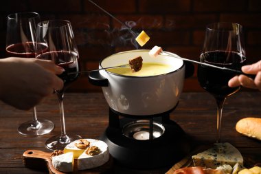 Kadınlar farklı aperatifleri fondü tenceresine (caquelon) daldırıyor. Eritilmiş peynirle kapalı masa içinde, yakın plan.