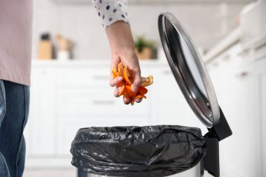 Mandalina kabuklarını mutfaktaki çöp kutusuna atan kadın, yakın plan.