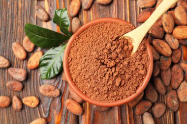 Doğal kakao çekirdekleri, toz ve yeşil yapraklar ahşap masada, düz yerde.