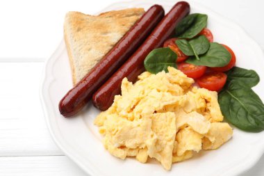 Lezzetli bir kahvaltı. Sosisli omlet, domates, ıspanak ve kızarmış ekmek beyaz ahşap masada, yakın plan.