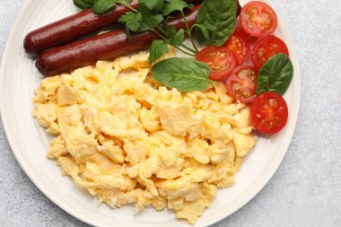 Lezzetli bir kahvaltı. Lezzetli çırpılmış yumurta, sosis ve domatesler gri desenli masa, üst manzara.