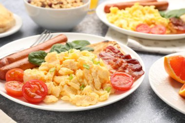 Lezzetli bir kahvaltı. Lezzetli omlet, pastırma, sosis ve domates. Gri desenli masada servis ediliyor. Yakın plan.