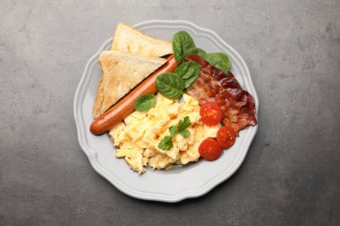Lezzetli bir kahvaltı. Lezzetli çırpılmış yumurta, domuz pastırması, sosis ve domatesler gri dokuma masasında servis edilir.