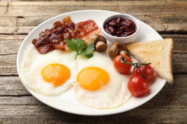 Geleneksel İngiliz kahvaltısı. Lezzetli, güneşli tarafı domuz pastırmalı, kırmızı fasulyeli, domatesli, mantarlı ve ahşap masada kızarmış ekmekli, yakın plan.