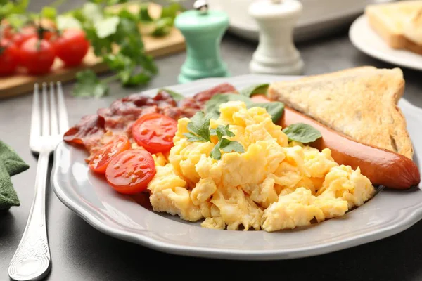 Lezzetli bir kahvaltı. Gri masada servis edilen domuz pastırmalı, sosisli ve domatesli nefis omlet, yakın plan.