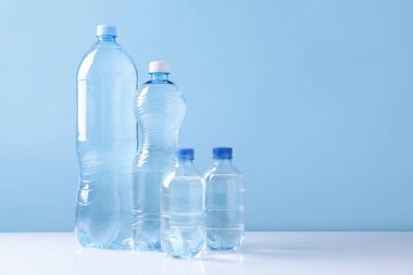 Beyaz masada açık mavi arka planda farklı boyutlarda su şişeleri var. Metin için boşluk