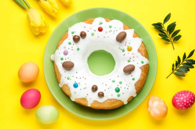 Lezzetli Paskalya pastası, boyanmış yumurtalar, güzel laleler ve sarı arka planda yeşil yapraklar.