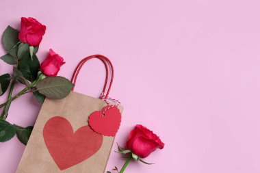 Kağıt torba ve pembe arka planda güller, düz yatış. Metin için boşluk