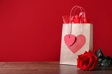 Kağıt torba ve gül kırmızı arka plana karşı ahşap masada. Metin için boşluk