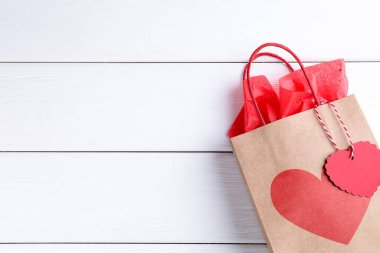 Beyaz ahşap arka planda kalbi olan hediye çantası, üst görünüm ve metin için yer. Sevgililer Günü