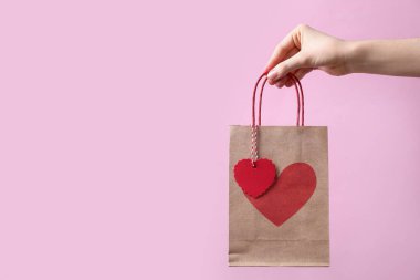 Kadının elinde pembe arka planda kalbi olan bir hediye çantası, yakın plan ve mesaj için yer var. Sevgililer Günü