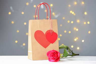 Beyaz ahşap masa üzerinde gül ile kağıt torba Gri arka plan ile bulanık ışık