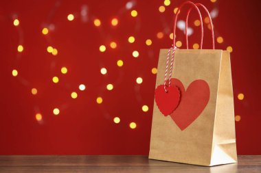 Tahta masada, kırmızı arka planda, üzerinde kalp izi olan, bulanık ışıklarla dolu bir kese kağıdı. Metin için boşluk