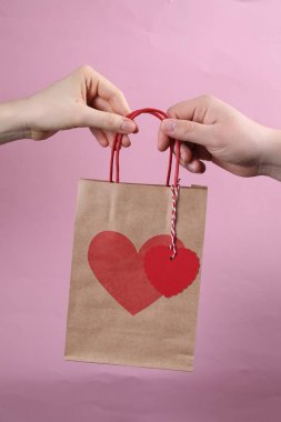 Sevgililer Günü hediyesi pembe arka planda olan kadın kesekağıdı veren adam, yakın plan.