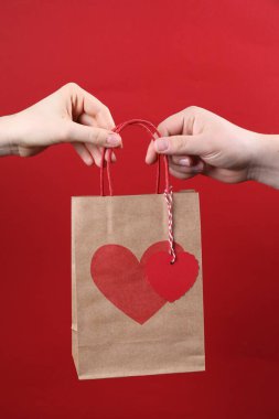 Erkek, kırmızı arka planda sevgililer günü hediyesi olan kağıt torbayı kadına veriyor.