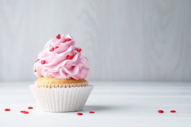 Sevgililer Günün kutlu olsun. Gri duvarın yanındaki beyaz ahşap masada kalp şeklinde serpiştirilmiş lezzetli kek, yakın plan. Metin için boşluk
