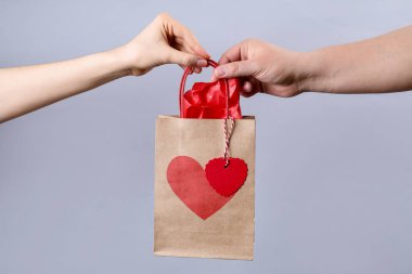 Erkek, sevgililer günü hediyesiyle arka plan aydınlatmasına karşı kadın kesekâğıdı veriyor.