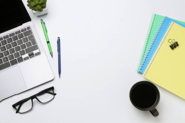 Ofis işyeri. Kırtasiye malzemeleri, dizüstü bilgisayar, bardaklar, kahve ve beyaz arka planda çiçek dekoru, düz yatak. Metin için boşluk