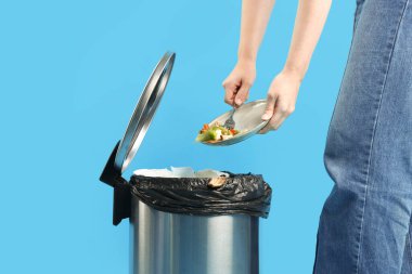 Açık mavi arka planda çöp tenekesine yemek atan kadın, yakın plan.