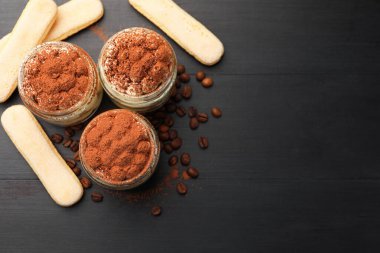 Kavanozlarda nefis tiramisu, savoiardi bisküvileri ve koyu ahşap masa üzerinde kahve çekirdekleri. Metin için boşluk