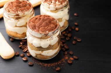 Kavanozlarda nefis tiramisu, Savoiardi bisküvileri ve koyu ahşap masada kahve çekirdekleri, yakın plan. Metin için boşluk