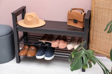 Evin içinde tozlu pembe duvarın yanında farklı ayakkabı ve aksesuarlarla dolu ayakkabı deposu.