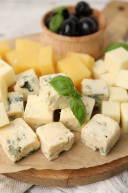 Açık ahşap masada değişik peynir, zeytin ve fesleğen içeren servis masası, yakın plan.