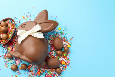 Çikolatalı Paskalya tavşanı, şekerli yumurta ve açık mavi arka planda serpiştirilmiş çikolata, düz yatak. Metin için boşluk